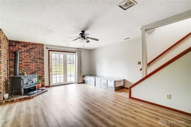 unfurnished living room featuring baseboards, wood finished floors, a wood stove, and a ceiling fan