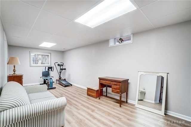 workout area with light wood finished floors, a paneled ceiling, and baseboards