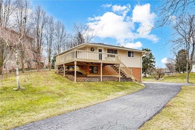 view of front of property with brick siding, a front yard, driveway, a wooden deck, and stairs