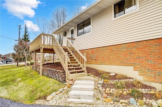 view of exterior entry with a yard, brick siding, and a wooden deck