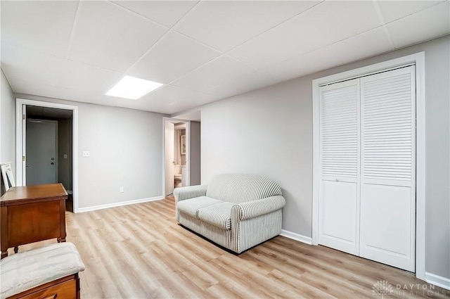 living area with a paneled ceiling, light wood finished floors, and baseboards