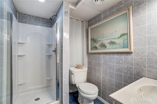 full bathroom with toilet, a stall shower, and tile walls