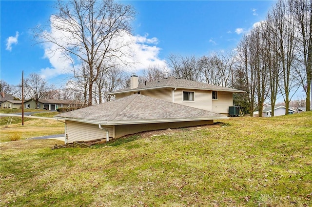 view of side of property with a shingled roof, cooling unit, a lawn, and a chimney