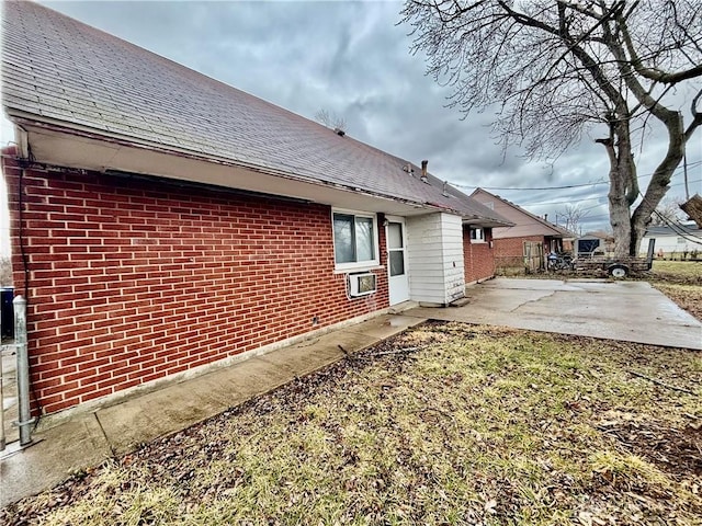 view of property exterior with brick siding, a shingled roof, and a patio