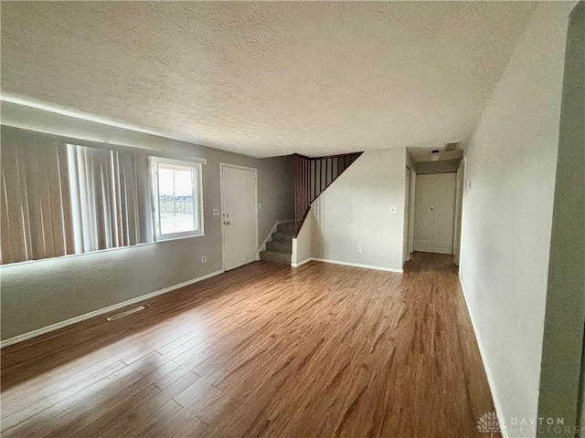 unfurnished living room featuring stairway, a textured ceiling, baseboards, and wood finished floors