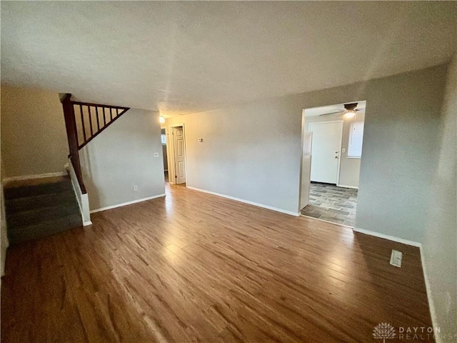 unfurnished living room with a ceiling fan, stairs, baseboards, and wood finished floors