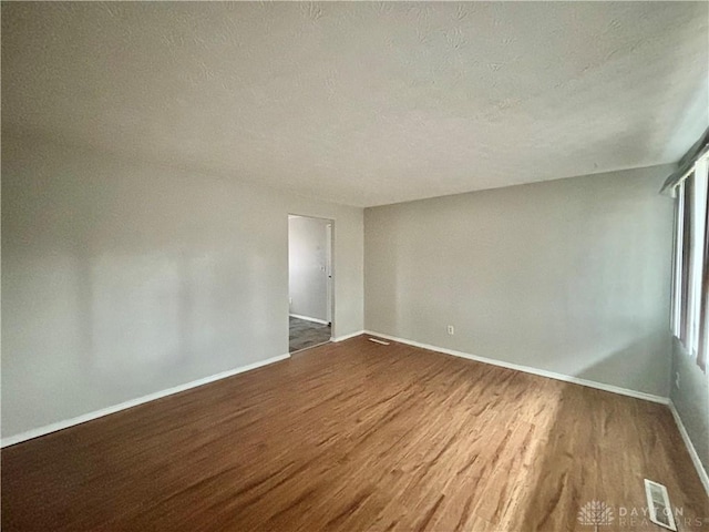 spare room with visible vents, a textured ceiling, baseboards, and wood finished floors