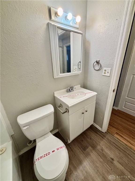 half bath with toilet, vanity, a textured wall, and wood finished floors