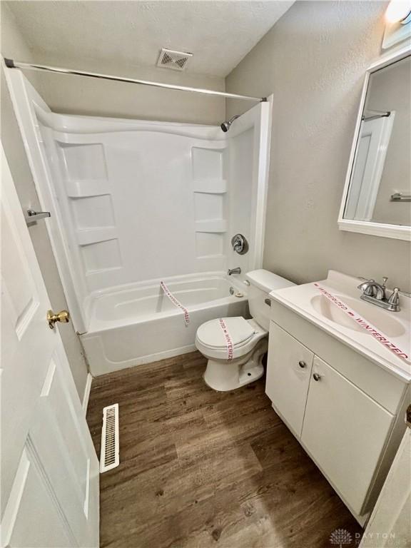 bathroom with visible vents, toilet, wood finished floors, vanity, and  shower combination