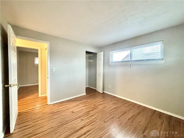 unfurnished bedroom with a closet, baseboards, a textured ceiling, and wood finished floors