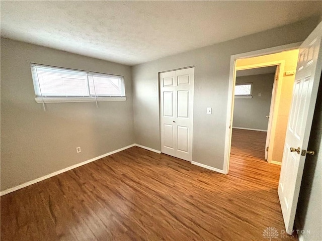 unfurnished bedroom featuring wood finished floors, baseboards, a closet, and a textured ceiling