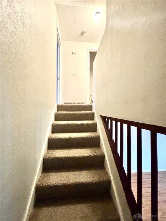 stairs with baseboards, a textured ceiling, and a textured wall