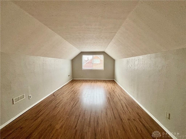 bonus room with wood finished floors, baseboards, visible vents, vaulted ceiling, and a textured ceiling