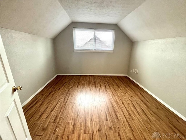 bonus room featuring lofted ceiling, wood finished floors, baseboards, and a textured ceiling