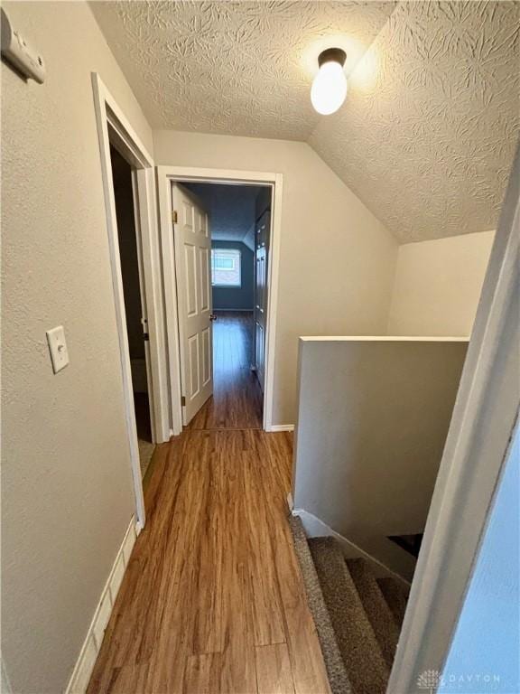 hallway with vaulted ceiling, a textured ceiling, baseboards, and wood finished floors