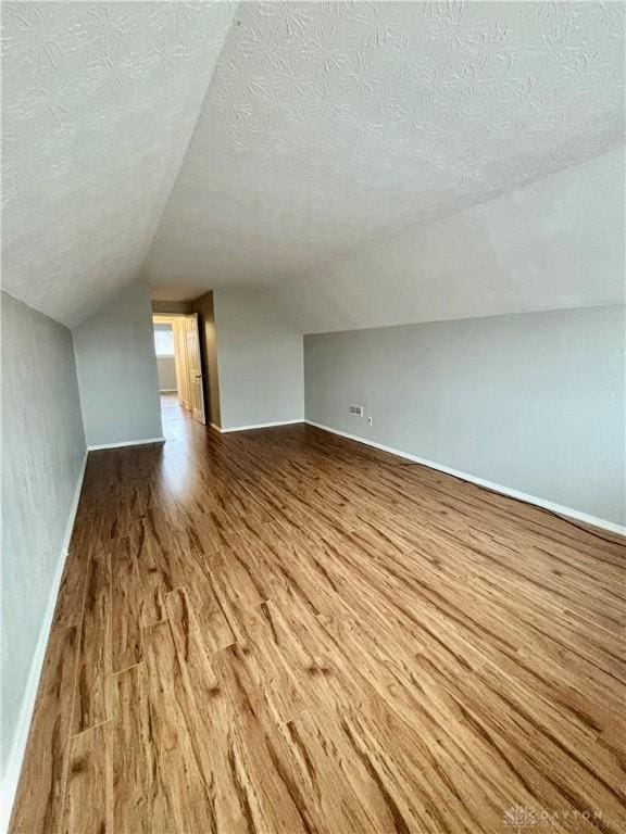 additional living space featuring baseboards, a textured ceiling, wood finished floors, and vaulted ceiling