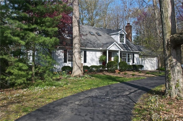 cape cod home with an attached garage, roof with shingles, and a chimney