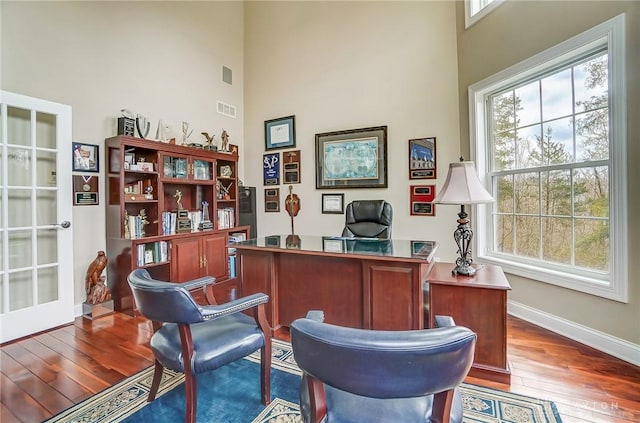 home office featuring a healthy amount of sunlight, hardwood / wood-style flooring, a high ceiling, and visible vents