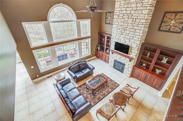 living area with a stone fireplace, tile patterned flooring, a high ceiling, a ceiling fan, and baseboards