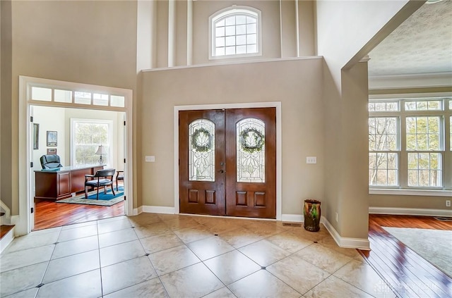 entrance foyer with a towering ceiling, light tile patterned floors, baseboards, and french doors