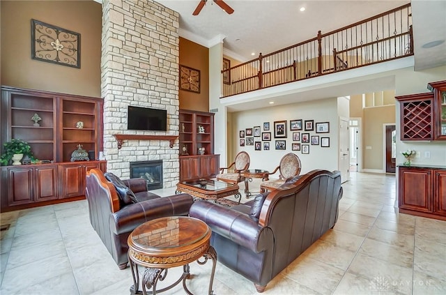 living area featuring ceiling fan, a stone fireplace, a high ceiling, baseboards, and crown molding