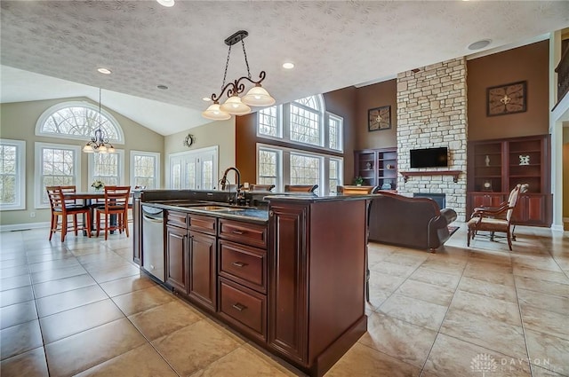 kitchen featuring dishwasher, dark countertops, a textured ceiling, a stone fireplace, and a sink