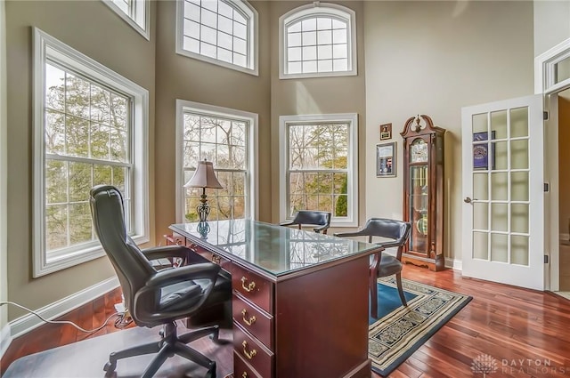 office area featuring plenty of natural light, a high ceiling, baseboards, and dark wood-type flooring