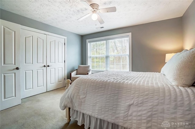 carpeted bedroom featuring a ceiling fan, a closet, visible vents, and a textured ceiling