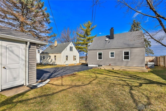 rear view of property with a lawn, a chimney, an outbuilding, fence, and a patio area