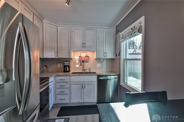 kitchen featuring light stone counters, decorative backsplash, appliances with stainless steel finishes, a sink, and wood finished floors