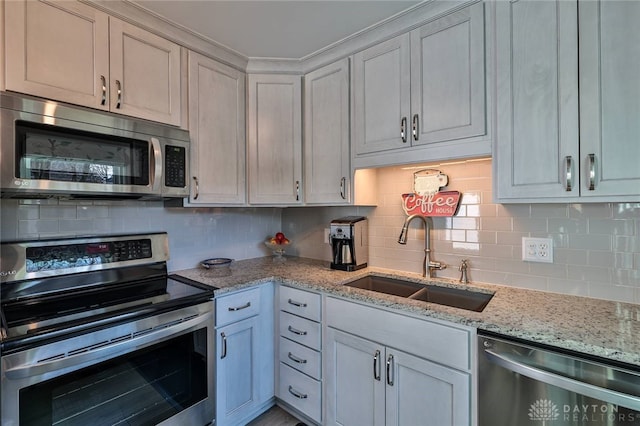 kitchen featuring stainless steel appliances, backsplash, a sink, and light stone countertops