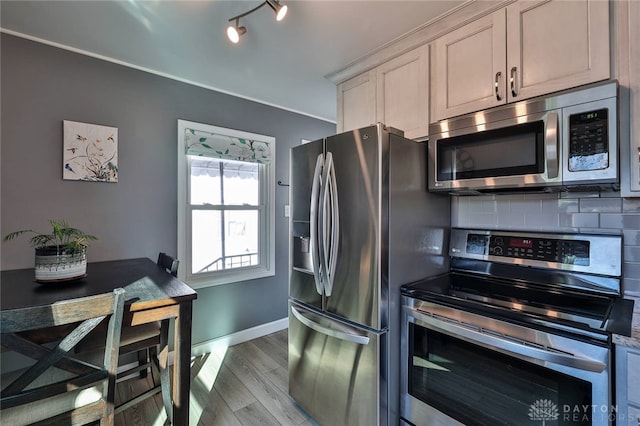 kitchen with light wood-style flooring, baseboards, appliances with stainless steel finishes, decorative backsplash, and track lighting