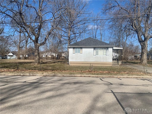 view of side of home featuring a yard, a fenced front yard, and roof with shingles