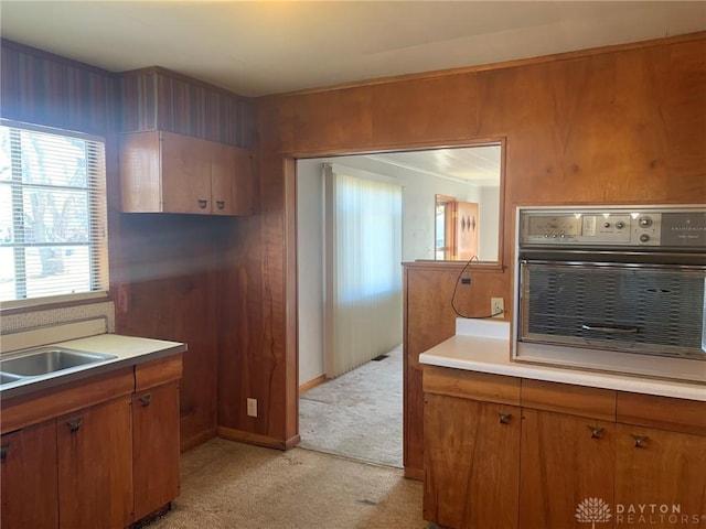 kitchen with oven, light carpet, a sink, light countertops, and brown cabinetry