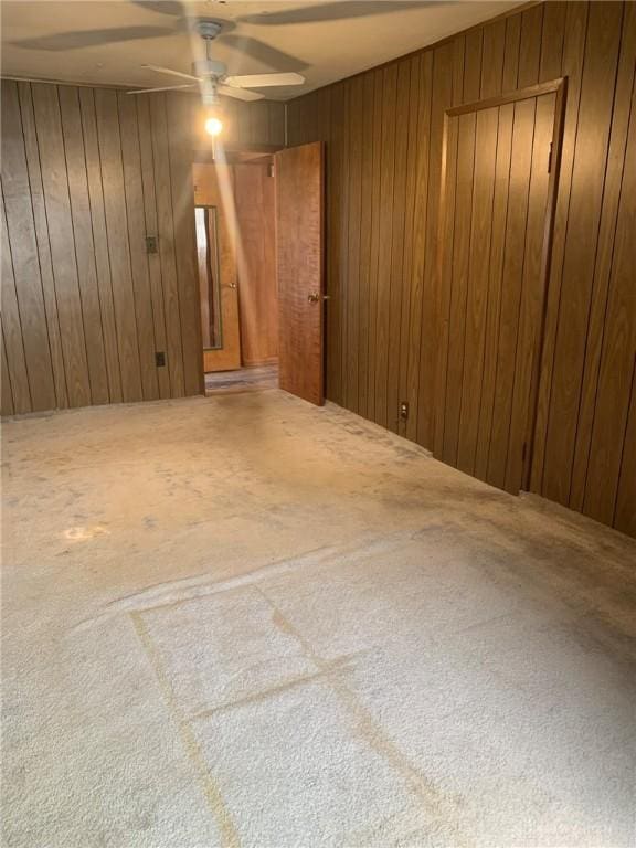 unfurnished room with carpet floors, ceiling fan, and wooden walls