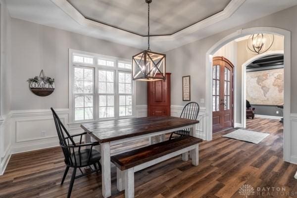 dining room featuring a raised ceiling, arched walkways, wainscoting, and dark wood-style flooring