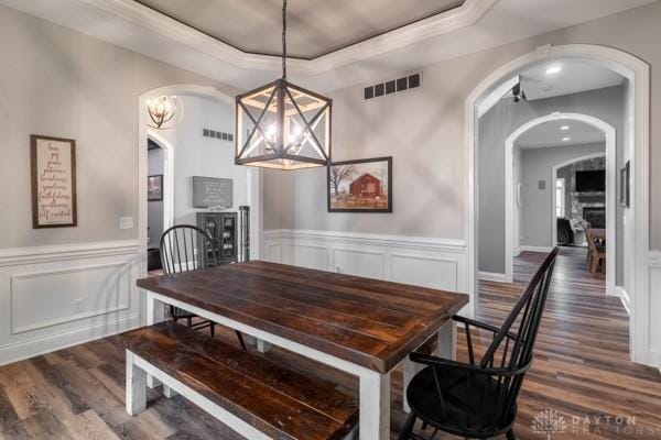 dining area featuring a tray ceiling, visible vents, arched walkways, and dark wood finished floors