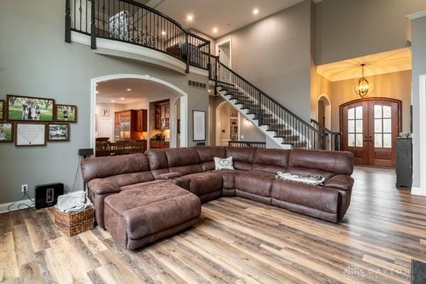 living room featuring stairway, french doors, a high ceiling, wood finished floors, and arched walkways