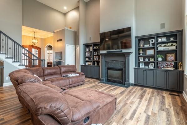 living room with a fireplace with flush hearth, wood finished floors, baseboards, a towering ceiling, and stairs