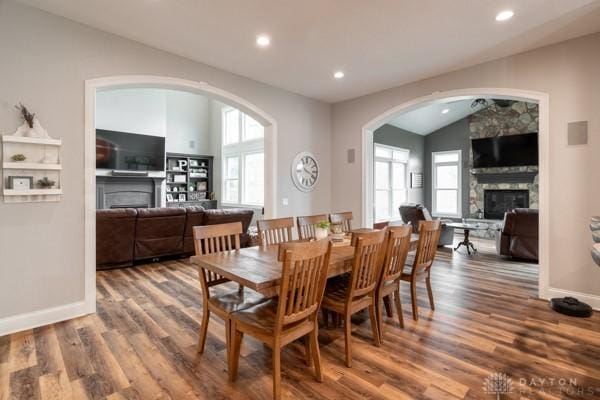 dining area with baseboards, lofted ceiling, a stone fireplace, recessed lighting, and wood finished floors