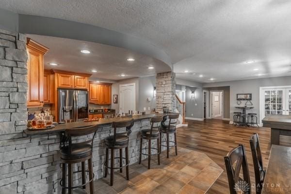 interior space with black fridge with ice dispenser, a textured ceiling, wood finished floors, recessed lighting, and baseboards