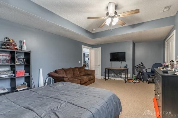 bedroom with visible vents, a tray ceiling, carpet floors, a textured ceiling, and a ceiling fan