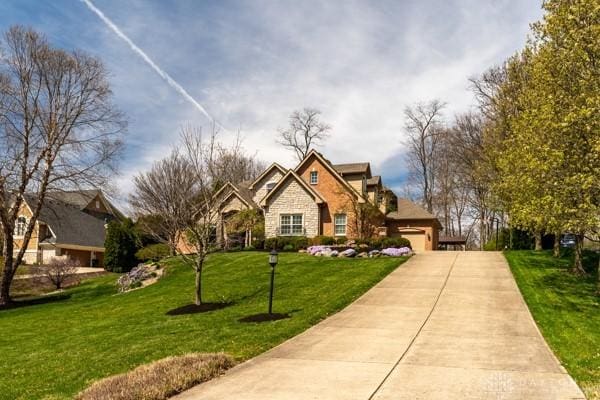 view of front of home featuring a garage, stone siding, concrete driveway, and a front lawn