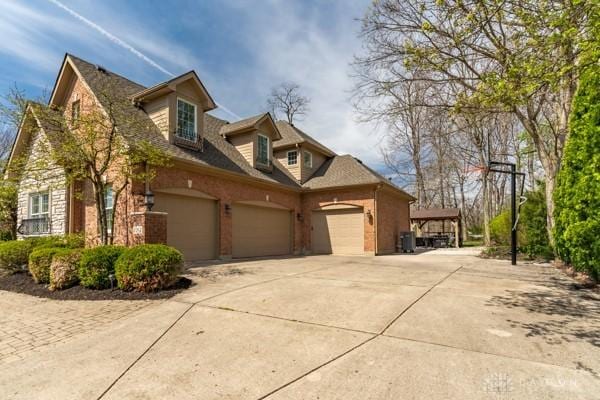 view of side of home with stone siding, central AC unit, driveway, and a garage