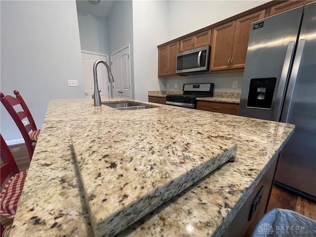 kitchen with light stone countertops, a kitchen island with sink, appliances with stainless steel finishes, and a sink