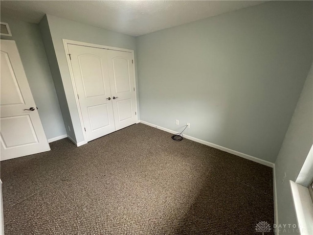 unfurnished bedroom with dark colored carpet, a closet, baseboards, and visible vents