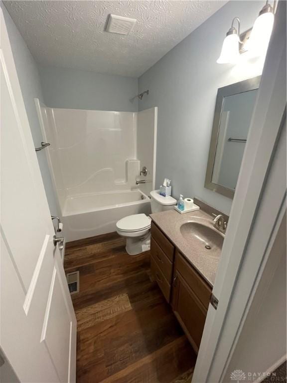 bathroom with toilet, shower / bathtub combination, wood finished floors, a textured ceiling, and vanity