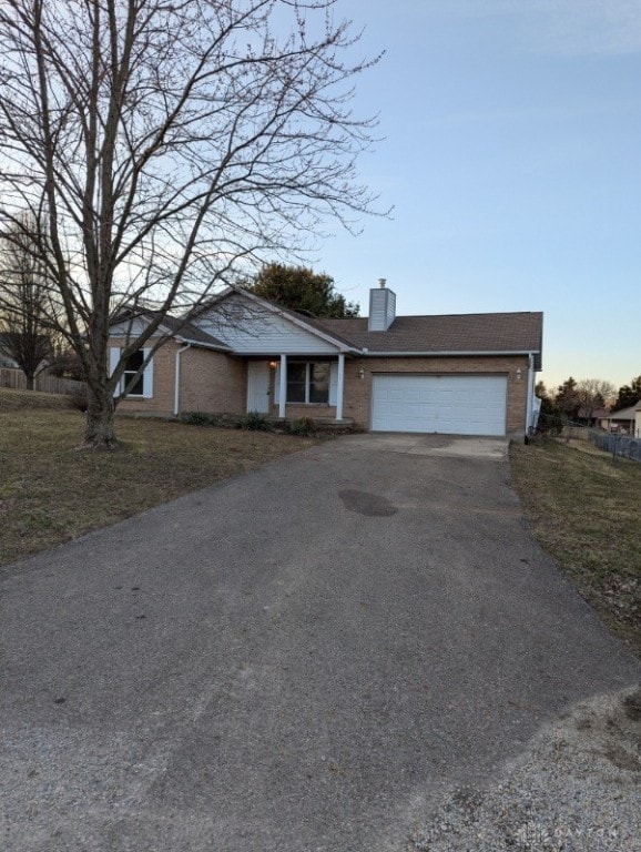 single story home featuring an attached garage, brick siding, driveway, and a chimney