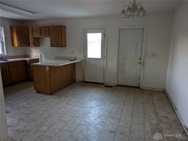 kitchen with brown cabinetry, light floors, a sink, light countertops, and a chandelier