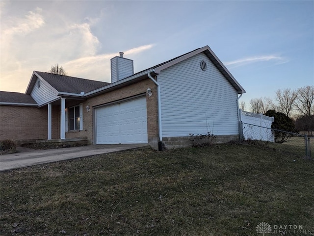 view of side of property featuring a lawn, driveway, fence, an attached garage, and a chimney